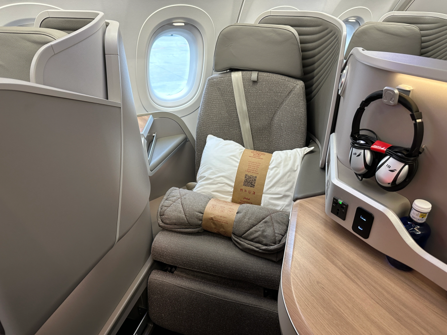 Vue intérieure du siège de classe d'affaires Airbus A321LR d'Etihad avec un design en peluche avec un oreiller et une couverture, aux côtés d'un écran tactile personnel et d'un casque.