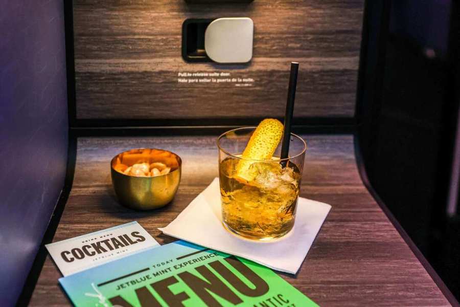 Un gros plan d'une configuration de divertissement en vol avec un verre de cocktail avec une garniture, un bol de collations et un menu sur une table dans une cabine d'avion.
